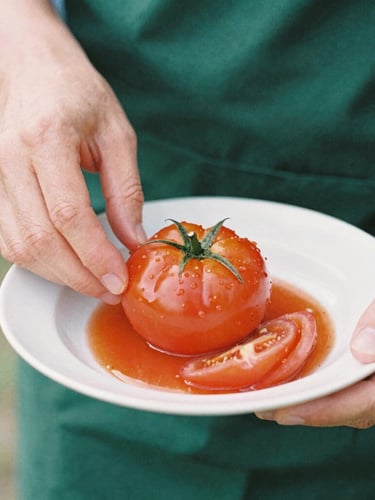 Close-up of hands carefully plating a vibrant heirloom tomato dish, soft natural daylight, shallow depth of field, 35mm film style