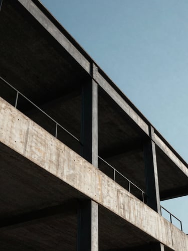 Vista en ángulo contrapicado de una imponente estructura de hormigón visto y vigas de acero negro bajo una luz solar intensa que genera sombras geométricas limpias.