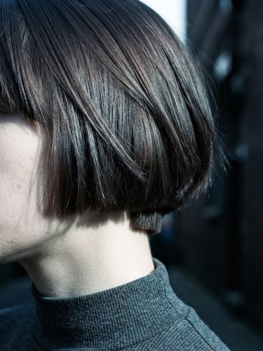 Stark close-up of a sharp geometric bob cut, high-contrast directional daylight, cool desaturated tones, showing hair texture and precise weight removal, 35mm film grain