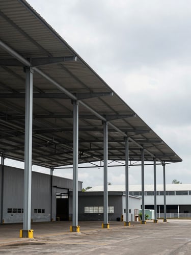 Environmental wide shot of a large finished industrial warehouse with metal roof and steel columns, photographed from outside at ground level, overcast daylight, Joinville industrial district visible in the background, no people