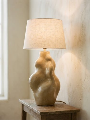 Large portrait photograph of a sculptural ceramic lamp in warm tones, casting soft shadows on a textured cream wall, diffused daylight from a large window, minimalist composition, shallow depth of field, 35mm.