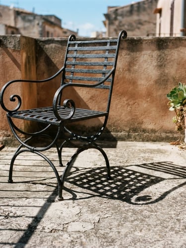 Architectural editorial crop of a heavy charcoal iron balcony chair, casting sharp geometric shadows on weathered concrete, warm terracotta accent tones, 35mm photography