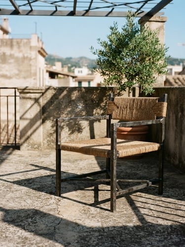 Architectural editorial photography of a heavy charcoal iron accent chair on a weathered concrete balcony, sharp afternoon sunlight casting geometric shadows, 35mm