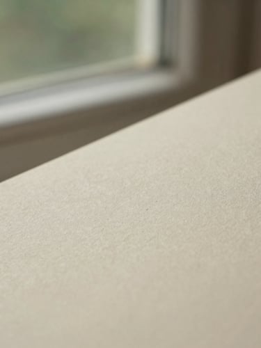 Macro close-up of soft textured paper under warm morning window light, shallow depth of field, muted cream tones