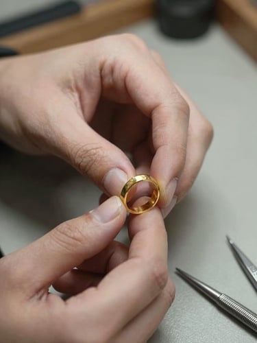 Close-up of a jeweler's hands holding a partially formed gold ring over a workbench, soft north-facing daylight illuminating the raw metal and the fine tools resting nearby