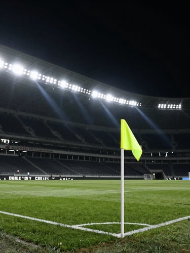 Dramatic stadium floodlights cutting through dark night sky, soccer field corner flag in focus, high-contrast sports photography.