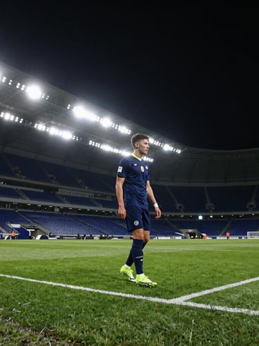 Wide dramatic stadium angle at night, football boots on wet turf under sharp spotlights, deep athletic navy tones.