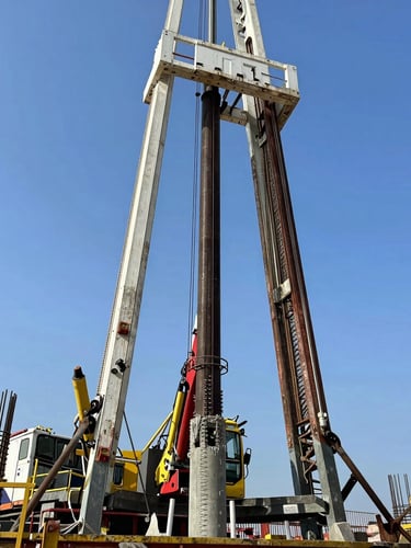 Medium shot of a drilling rig pouring concrete into a freshly drilled shaft, steel reinforcement cage visible, high-contrast industrial construction photography.