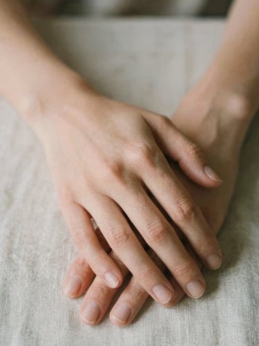 Close-up of hands gently resting on a textured linen cloth, soft diffused daylight, warm editorial photography, shallow depth of field