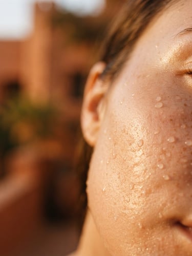Macro close-up of glowing skin with soft golden hour light, water droplets, rich terracotta background, shallow depth of field, 35mm