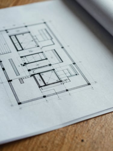 Close-up macro shot of architectural blueprints and industrial print materials on a solid oak table, cool overcast daylight, 35mm film.