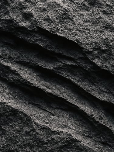 Extreme close-up of raw stone surface in cool gallery light, deep erosional marks and mineral grain visible, high contrast shadow geometry, no warmth, no styling, architectural framing