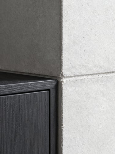 Close-up macro shot of a flawless architectural join, clean shadow-gap detailing between concrete wall and dark oak cabinet, natural side lighting, sharp shadows