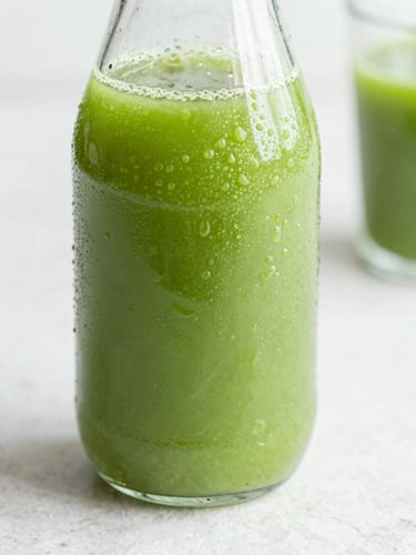 Macro close-up of a condensation-beaded glass bottle of vibrant green juice on a clean light stone surface, soft high-key natural daylight, 35mm