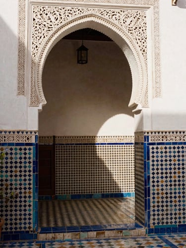 Warm editorial photography of a traditional Andalusian courtyard in Tetouan, intricate mosaic tilework, soft Moroccan sunlight filtering through an archway, 35mm