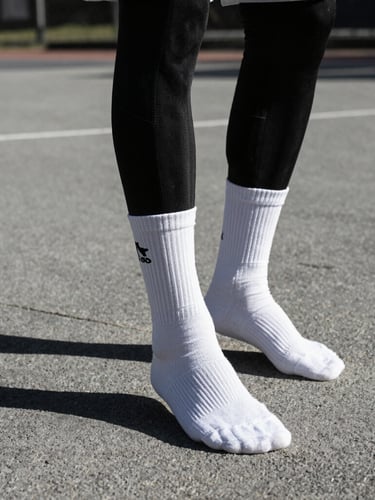 Low-angle action shot of a basketball player wearing custom black and white compression socks on an outdoor concrete court, dramatic sunlight with deep shadows