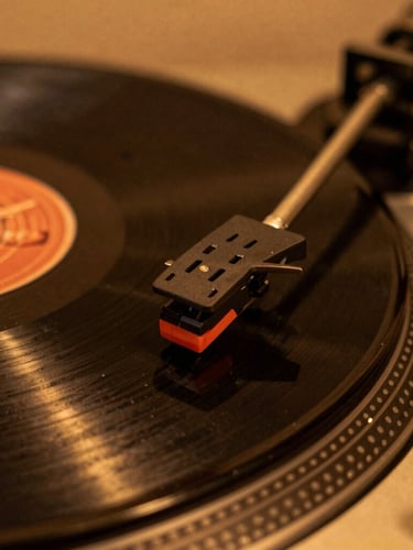 Close-up macro shot of a vintage turntable needle resting on a spinning vinyl record, warm low-key studio lighting with amber glow, shallow depth of field, 35mm