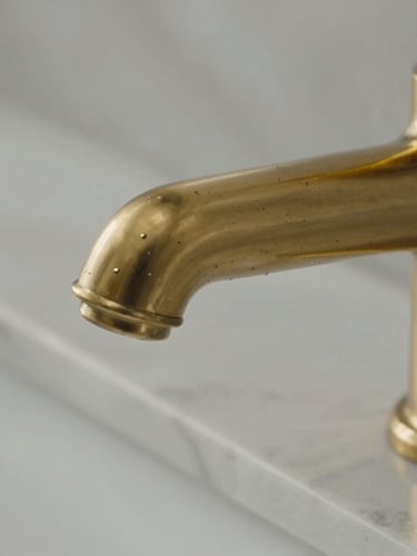 Macro detail of a pristine brass faucet and immaculate marble countertop, high-contrast side lighting highlighting the spotless, polished surface with zero water spots.