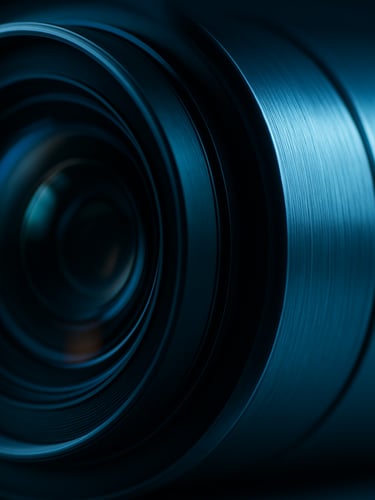 Macro close-up of a sleek camera lens reflection and brushed aluminum housing under cool blue studio lighting.