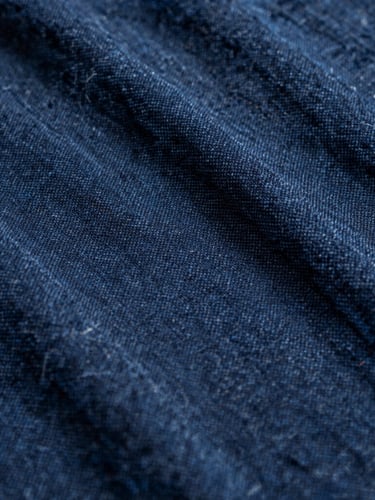 Macro texture of rich indigo dyed cotton fabric, warm natural side-light, showing intricate handloom weave details, 35mm photography