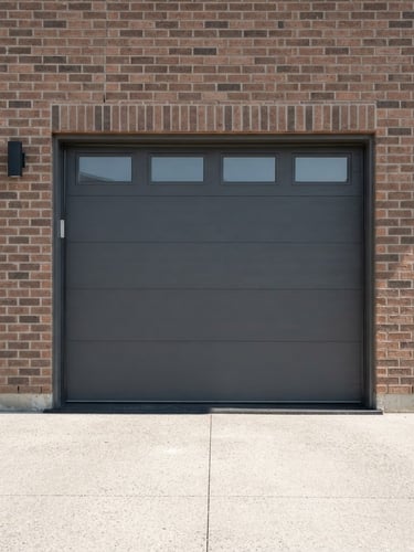 Straight-on exterior shot of a modern charcoal gray garage door installed on a brick suburban home, bright natural daylight, sharp focus