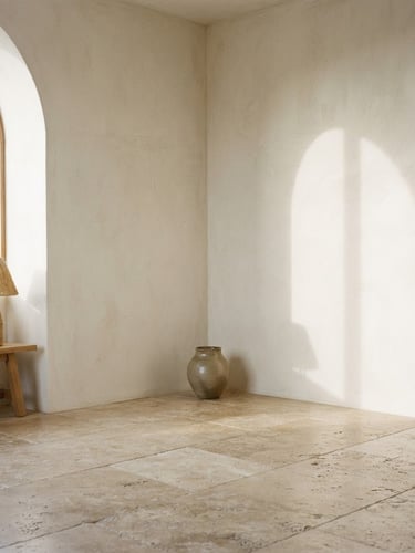 Straight-on architectural composition of a sun-drenched room corner, raw travertine floor, soft shadows on plaster walls, minimalist interior design, neutral earth tones, medium format film