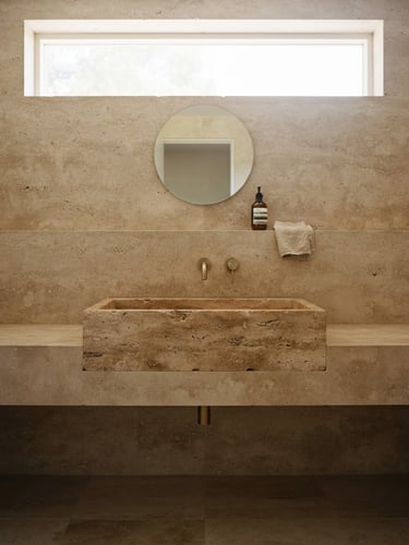 Straight-on architectural composition of a monolithic travertine bathroom basin, soft morning light filtering through a high window, neutral earth tones, medium format film.