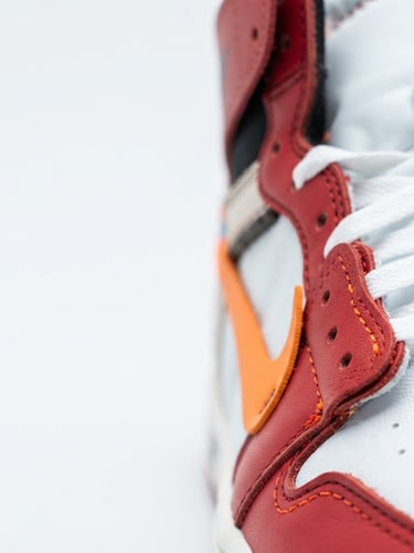 Tight macro shot of rare sneaker stitching, high-contrast studio lighting, clean white background, vibrant orange accents, 50mm lens, right third.