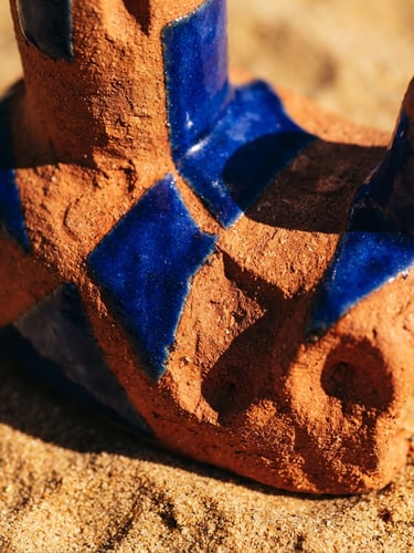 Extreme close-up of a vibrant terracotta and cobalt blue sculptural ceramic object on a warm sand background, hard direct sunlight casting dramatic sharp shadows, macro texture, 35mm lens