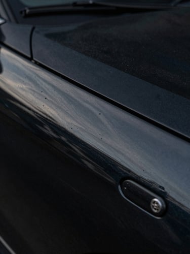 Extreme close-up of a deep-black automotive paint surface under diffused studio lighting, micro-detail of glossy reflection and paint clarity visible, no people, no text, edge-to-edge panel fill