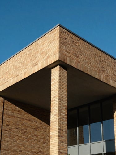 A sharp architectural detail of a modern university pavilion in Perth, sand-colored brickwork contrasting with bright blue sky, clean geometric lines.
