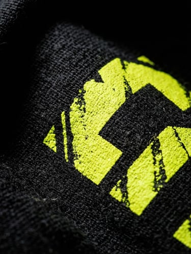 High-contrast urban product photography, macro shot of thick black cotton fabric with crisp screen printing in neon yellow, dramatic studio lighting, deep shadows, 35mm