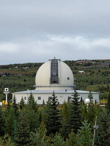Wide panoramic environmental shot of a remote meteorological research station in a sub-arctic landscape under cool, overcast daylight, with monitoring instruments visible.