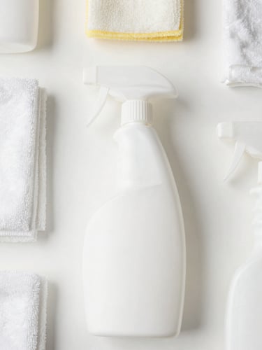 Top-down clean shot of neatly arranged professional cleaning tools, microfiber cloths, and spray bottles on a bright white surface, natural light, 35mm