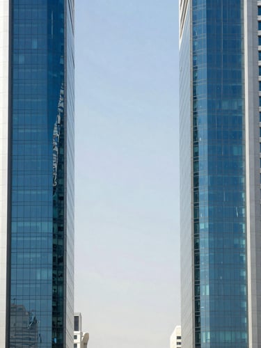 Symmetrical architectural perspective of a modern financial district skyscraper in Riyadh, steel and glass facade reflecting bright daylight, clean sharp shadows, cool blue and slate tones