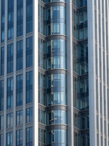 Symmetrical modern architectural perspective of a financial district skyscraper, clean steel and glass lines, bright natural daylight, cool blue and slate tones, sharp focus