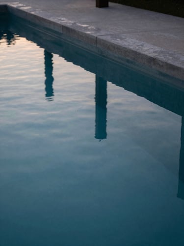 Extreme close-up of still, mirror-like water surface reflecting clean concrete lines of an architectural estate pool at twilight, minimal composition.