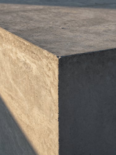 Close-up of finished textured concrete surface with crisp architectural edges, dramatic early morning golden hour light casting long shadows, 35mm.