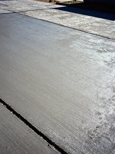 Low-angle heroic shot of freshly poured concrete driveway in Birmingham, Alabama, high-contrast midday sun highlighting the smooth hand-troweled texture, deep shadows, 35mm.