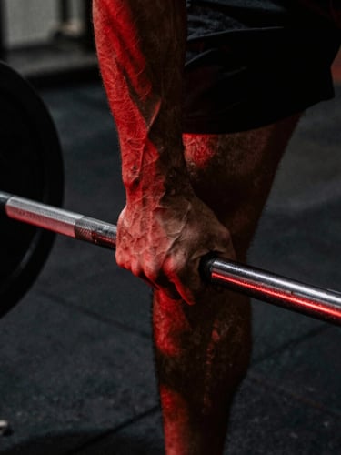 Close-up of a hand gripping a heavily knurled steel barbell in a dark, gritty warehouse gym, intense red rim light highlighting muscle definition, deep shadows, dramatic 35mm photography