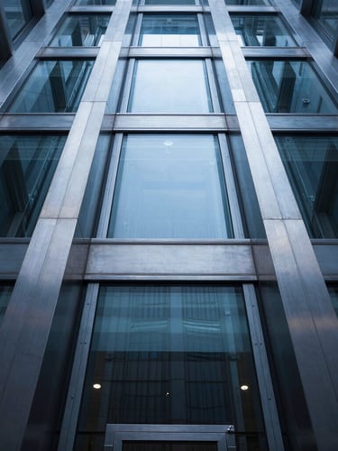 Low-angle architectural shot of a modern glass elevator shaft, cool crisp daylight reflecting on brushed steel rails, symmetrical composition.