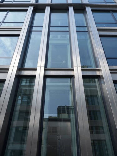 Symmetrical low-angle photograph of a modern glass residential elevator shaft, soft natural daylight reflecting on brushed steel, clean architectural lines.