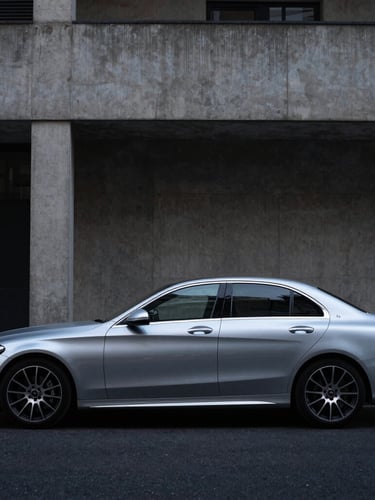 Wide-angle profile shot of a clean metallic silver Mercedes C-Class parked against a minimalist concrete architectural facade in South London, moody overcast daylight, 35mm lens