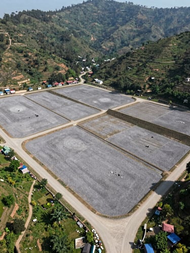 Wide-angle drone shot of structured land plotting in Kathmandu, showing clear boundary lines, gravel road access, and surrounding green hills under bright natural daylight.