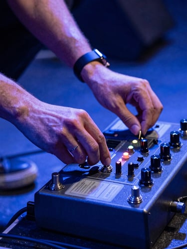 Close-up of hands adjusting a guitar pedalboard on a stage, dynamic Dutch angle, high-contrast blue stage lighting, energetic composition