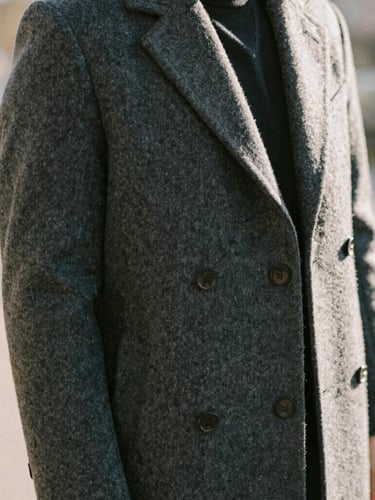 Warm editorial portrait of a professional in natural motion, wearing a structured charcoal wool overcoat, soft morning daylight, shallow depth of field, 35mm film style.
