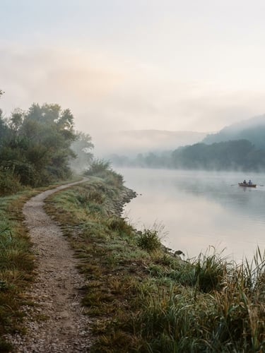 Soft morning mist over the wide Danube river, a narrow gravel path winding along the water edge, warm editorial 35mm photography