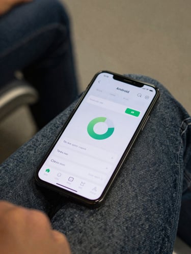 Android phone resting on a commuter's lap, screen showing a minimal battery-monitor app interface at actual resolution, ambient indoor transit lighting