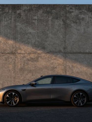 Low-key dramatic profile of a luxury electric sedan parked beside a textured concrete architectural wall at dusk, sharp shadows.