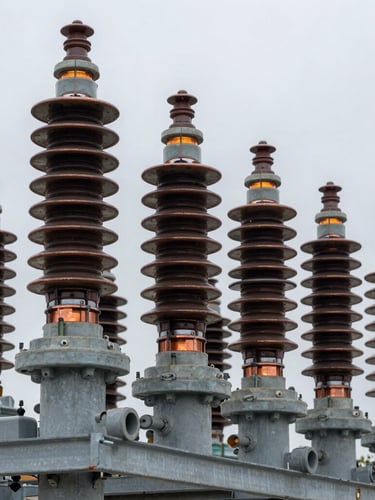 Close-up of heavy copper transformer windings and industrial ceramic insulators, overcast outdoor lighting, cool slate gray and safety amber tones, sharp technical detail, 50mm lens, industrial editorial photography